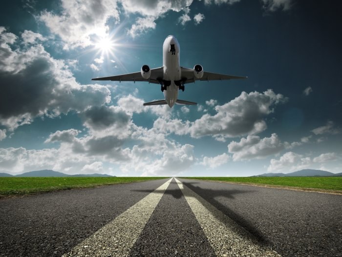 Airplane ascending above a runway with sun and clouds in the sky