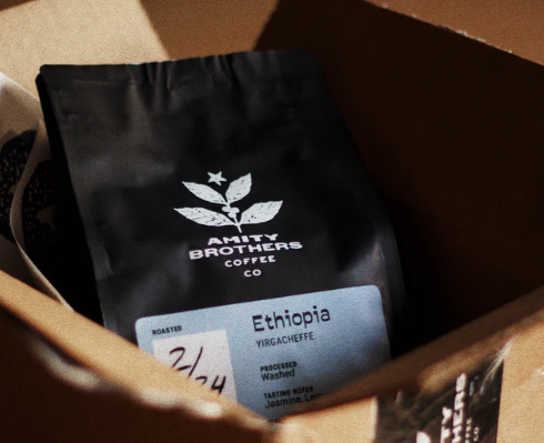 Black bag of Amity Brothers Ethiopia Yirgacheffe coffee sitting in a cardboard box under warm light