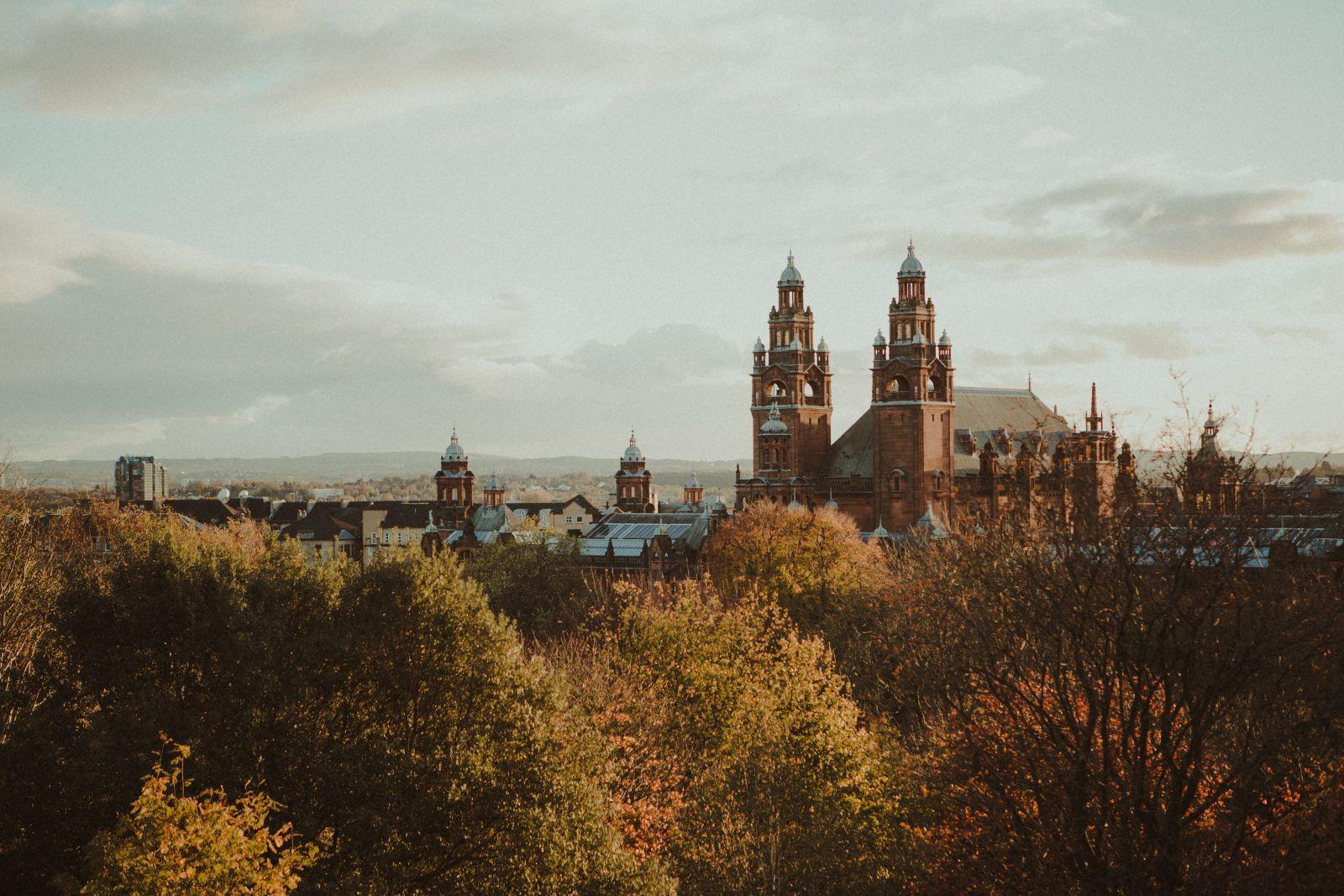 Historic building with towers behind a canopy of trees with autumn foliage under a cloudy sky