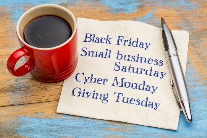 Red coffee mug and silver pen beside a napkin listing Black Friday, Small Business Saturday, Cyber Monday, and Giving Tuesday