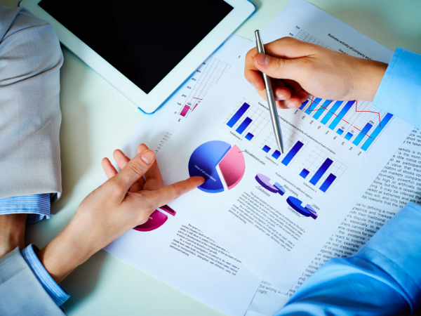 Two people discussing business charts and graphs on printed documents alongside a tablet