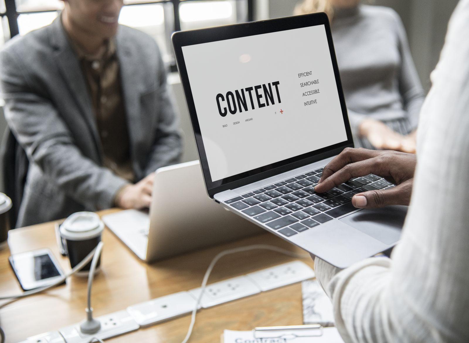 Person holding open laptop showing the word CONTENT with related terms on the screen in a meeting room