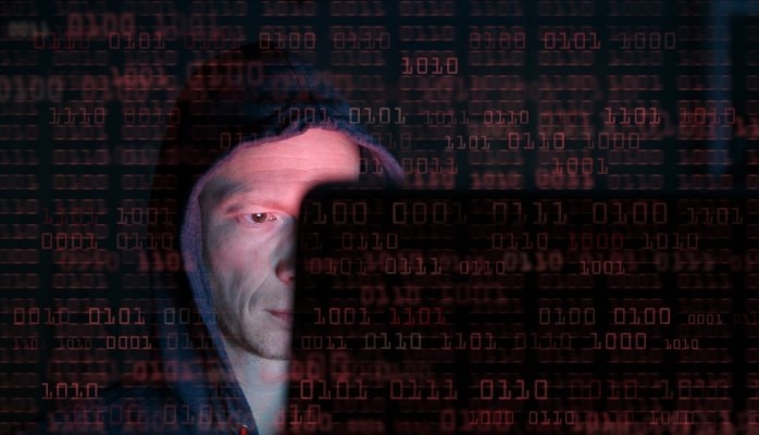 Cyber Crime News - Web Development Person in a hooded sweatshirt partially obscured by red digital binary code, symbolising cyber hacking and cybersecurity threats