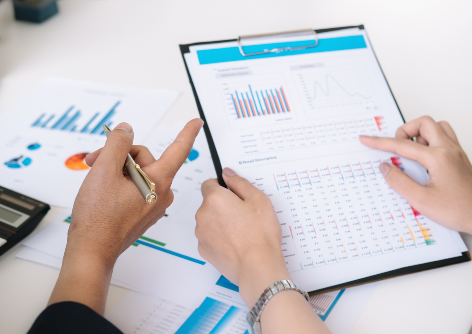 Hands pointing at printed sheets with charts and graphs, analysing data on a clipboard and other papers