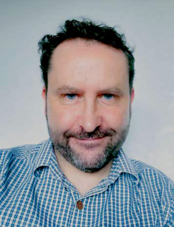 Head and shoulders portrait of a man with short dark hair and a beard wearing a checked shirt