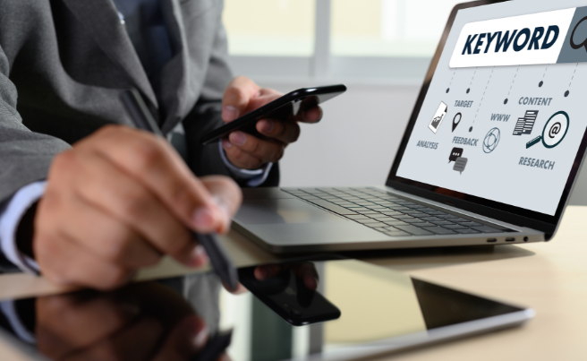 Person using a smartphone and stylus with a laptop displaying keyword analysis and SEO strategy icons