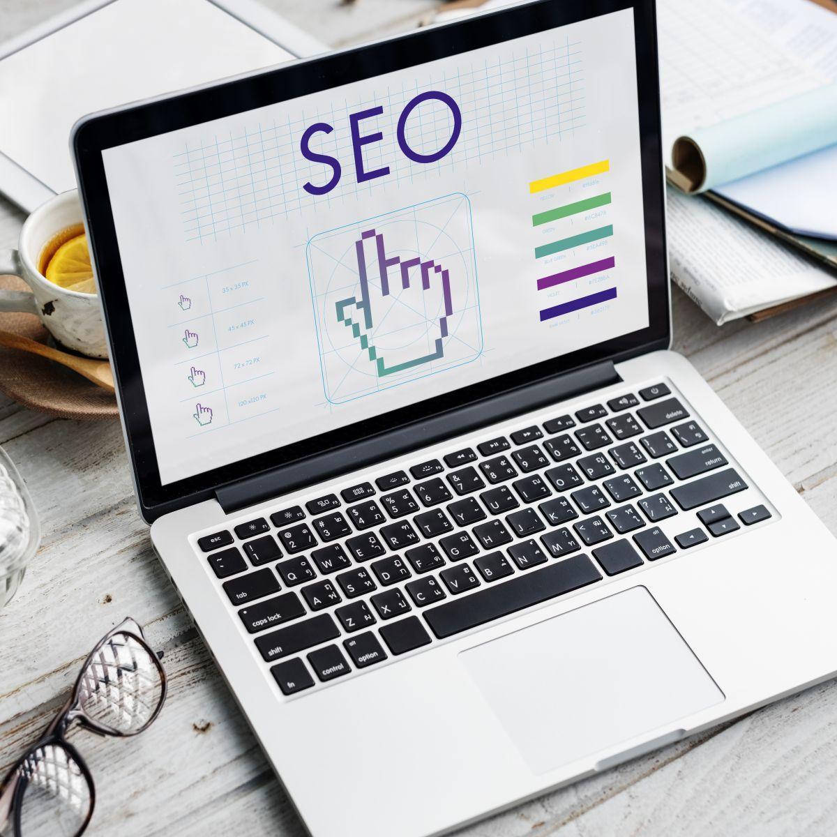 Laptop displaying a pixelated cursor hand icon and colour palette with the text SEO on screen