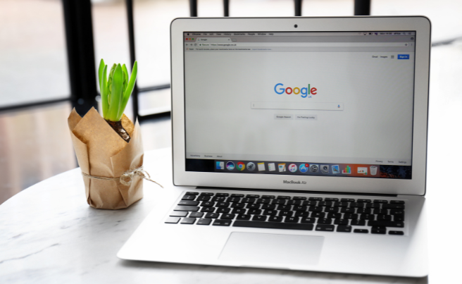 Open MacBook Air laptop displaying Google search page next to a small green plant wrapped in paper on a round white table