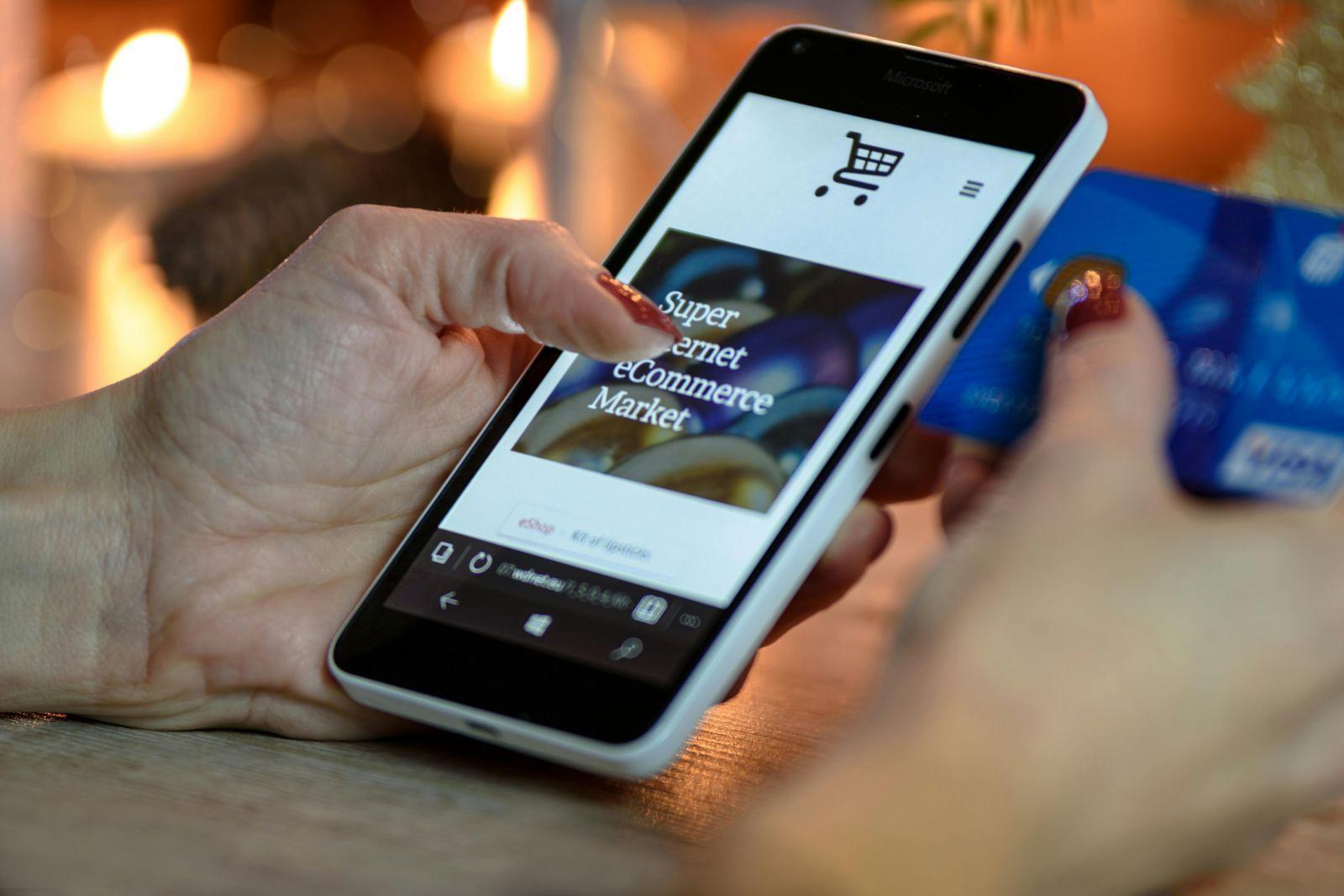 Person holding a smartphone displaying an online shopping page with text 'Super internet eCommerce Market' while holding a blue credit card