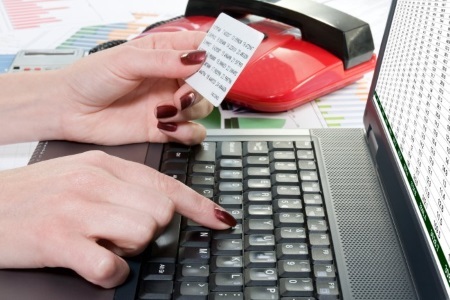 banking-safely-online Hands using a laptop keyboard while holding a banking card, with financial documents and a red calculator nearby
