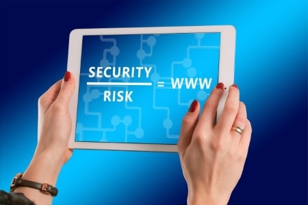 Safe-Business-Online Person holding tablet displaying a diagram linking security, risk and www on a blue digital background