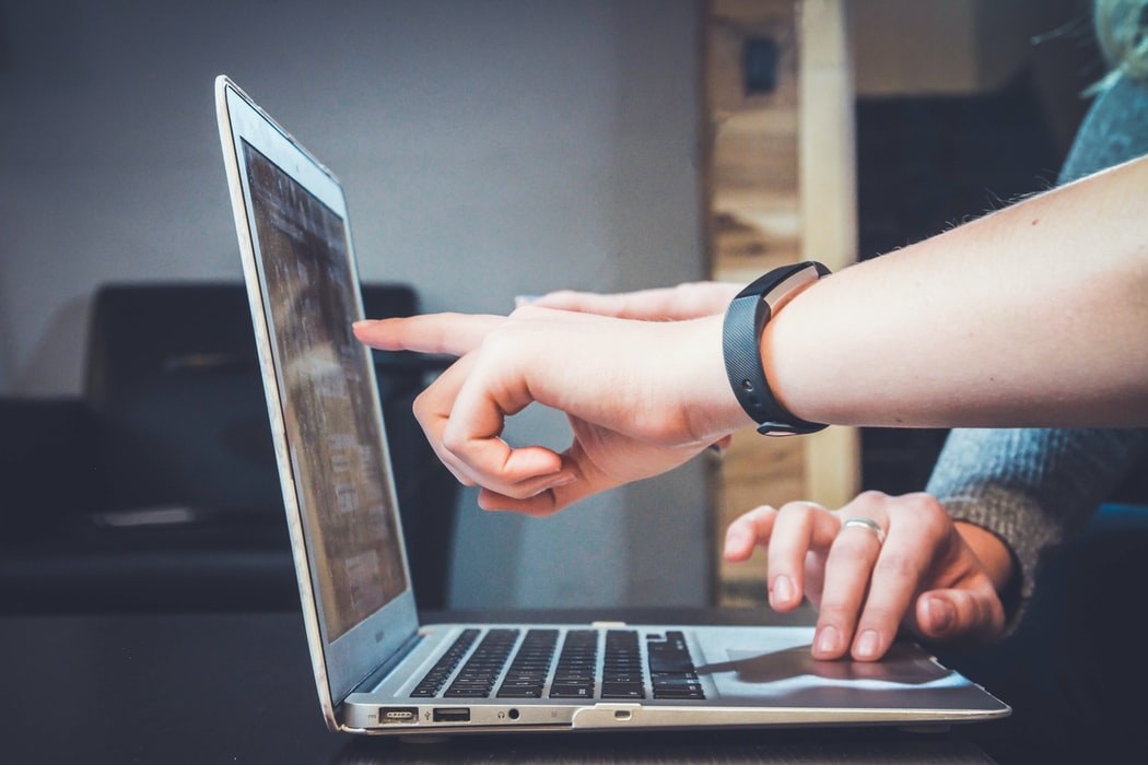 Hand pointing at a laptop screen while another person types on the keyboard