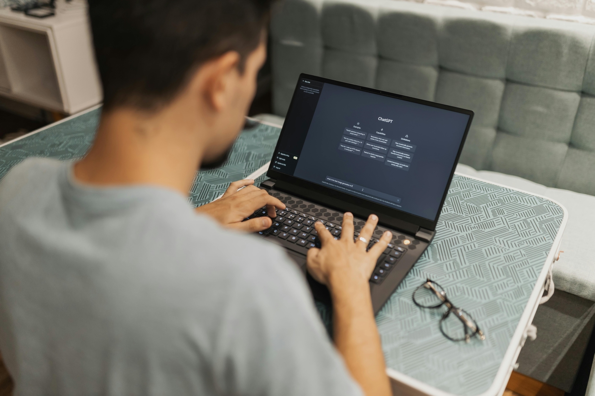 Person typing on a laptop displaying ChatGPT interface with examples, capabilities and limitations sections