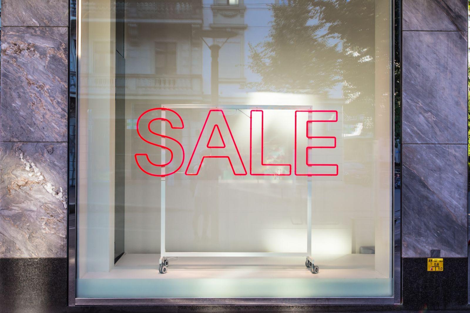 Red neon SALE sign displayed in a shop window with reflections of the street outside