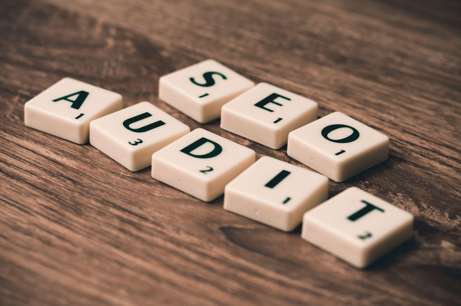 Scrabble tiles on a wooden surface forming the words SEO and AUDIT