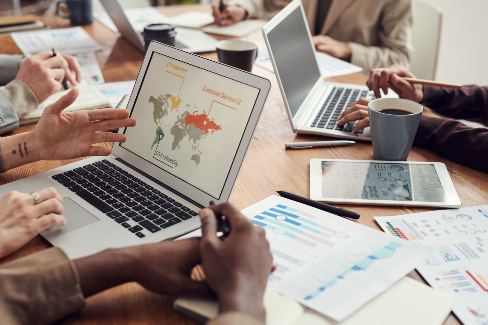 People in a meeting discussing business data displayed on laptops, including a world map with retention, customer service and profitability metrics