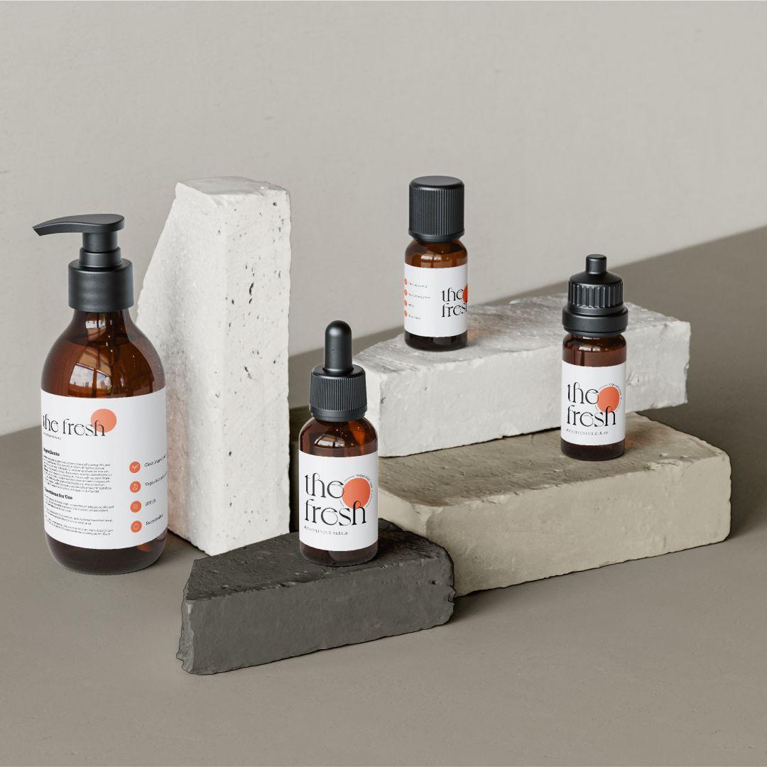 Four amber glass skincare bottles with black caps arranged on grey, white, and beige bricks against a neutral background