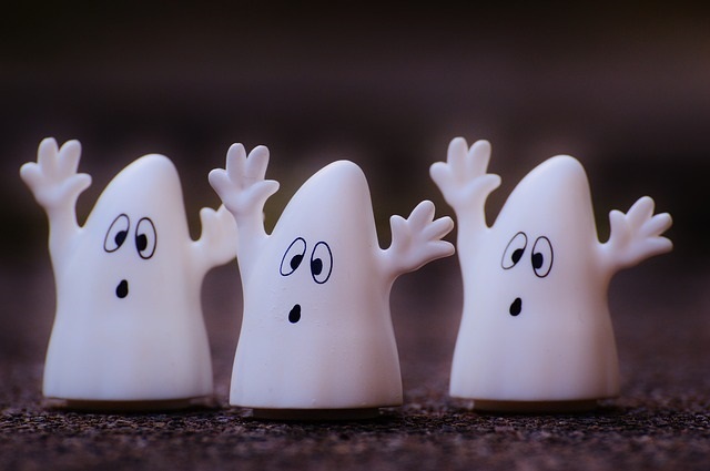 Three white ghost figurines with surprised expressions on a rough surface