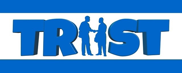 Blue 3D word 'TRUST' with silhouettes of two people shaking hands forming the letter U