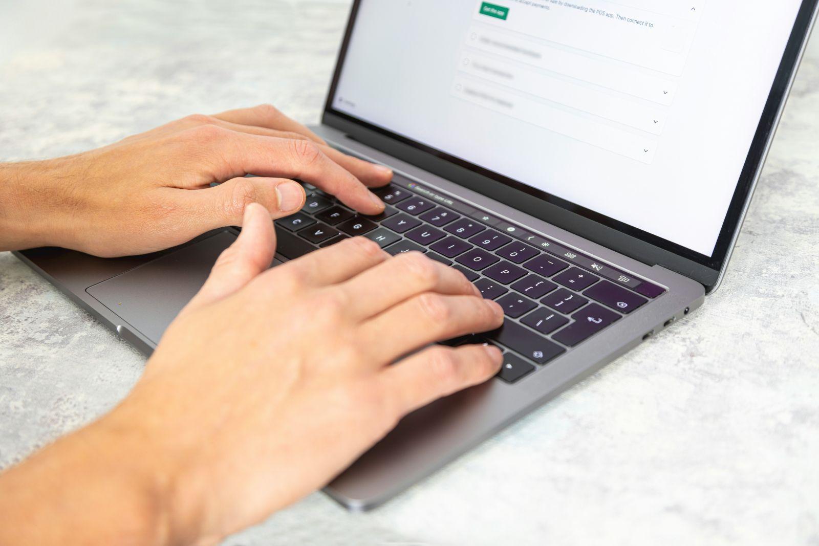 Close-up of hands typing on a laptop keyboard on a light surface