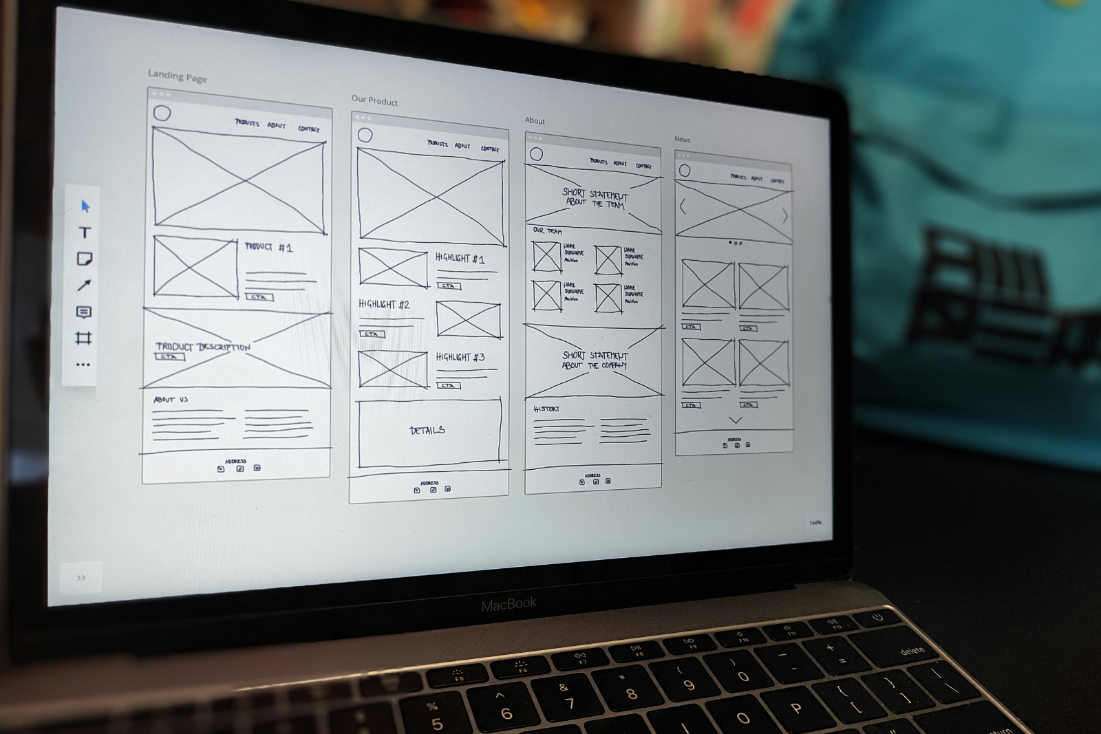 Hand-drawn UX wireframes displayed on a MacBook screen showing layouts for landing page, product, about, and news sections