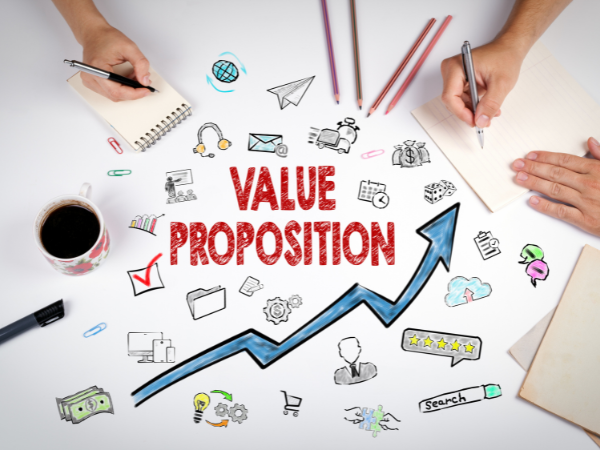 Hand-drawn business icons surrounding the words 'Value Proposition' with an upward arrow showing growth, alongside two people writing notes and a cup of coffee