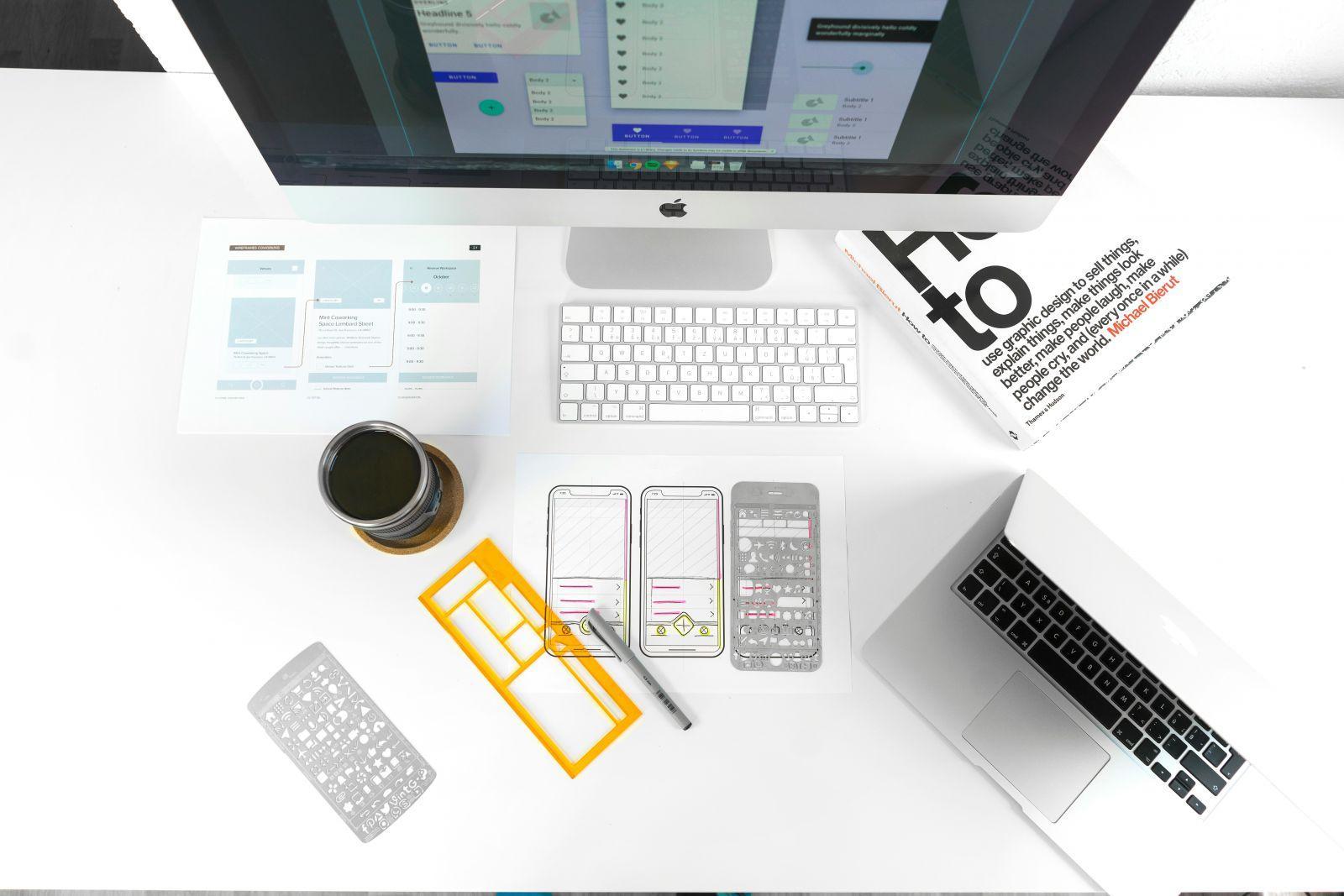 Workspace with computer, keyboard, laptop, graphic design templates for mobile apps, stencils, pen and a coffee cup