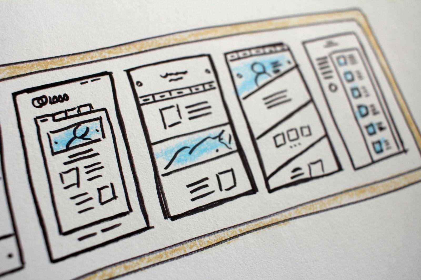 Close-up of a hand-drawn website wireframe sketch featuring multiple webpage layouts with text blocks and image placeholders in blue highlights