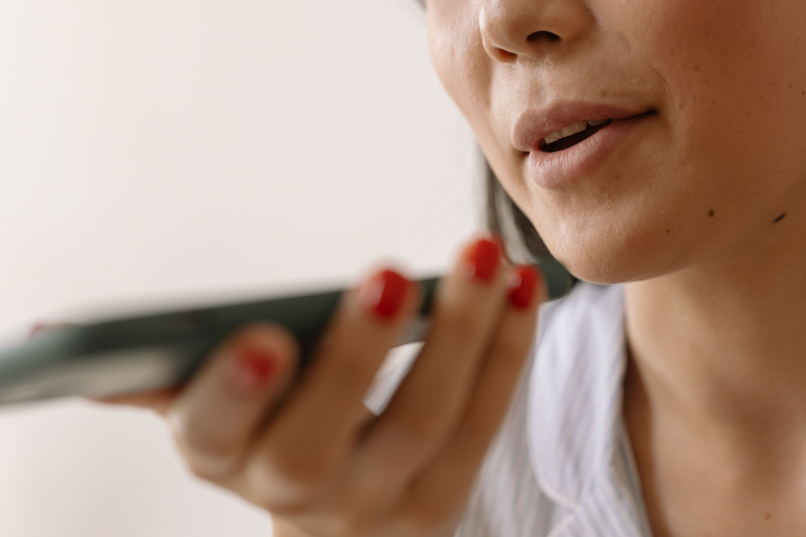 Close-up of a woman speaking to a smartphone with red nail polish visible on her fingers