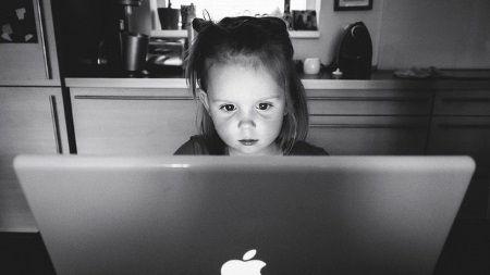 Young child looking intently at a laptop screen in a black-and-white kitchen scene.