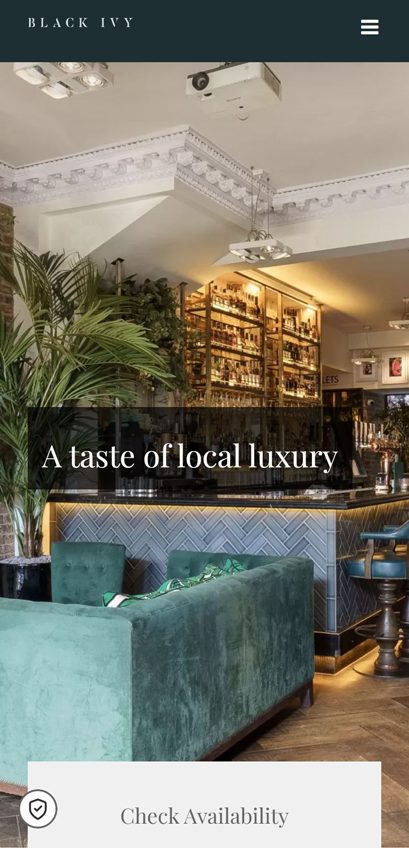 Luxurious bar interior with green velvet seating, decorative ceiling, and a well-stocked backlit bar area on Black Ivy website