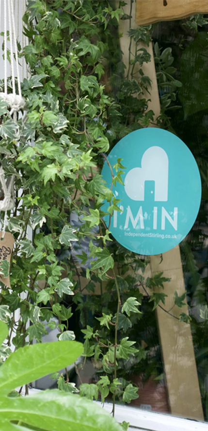 Independent Stirling logo sticker on a shop window surrounded by green ivy plants