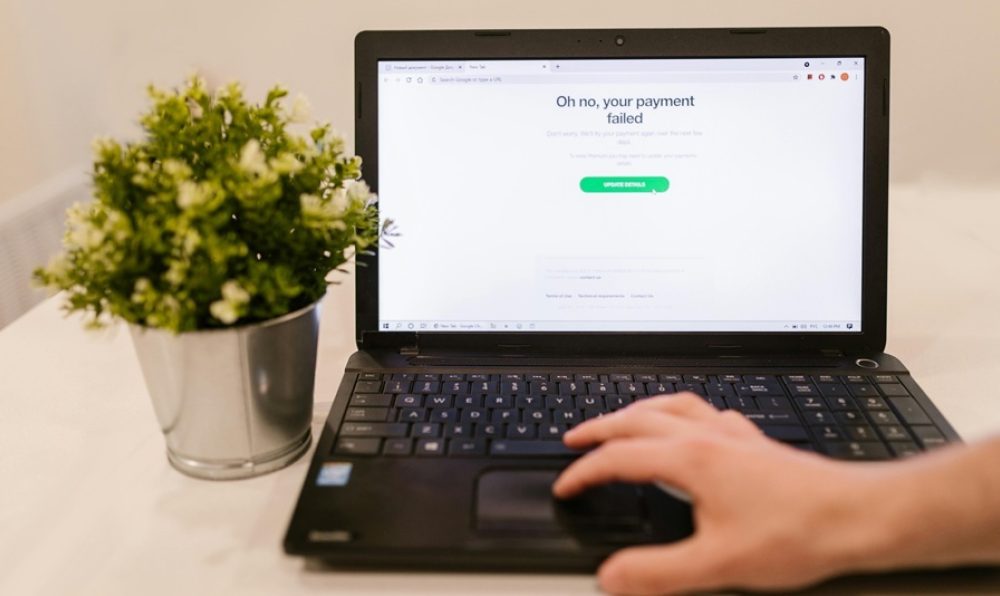 Open laptop showing a payment failed message on an eCommerce website with a hand on the keyboard and a potted plant nearby