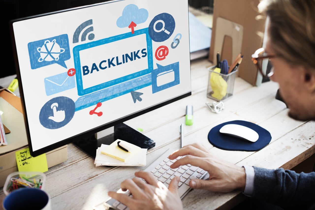 Person working on a desktop computer showing a digital illustration of SEO backlinks and related icons such as search, cloud upload, email, and sharing on the screen