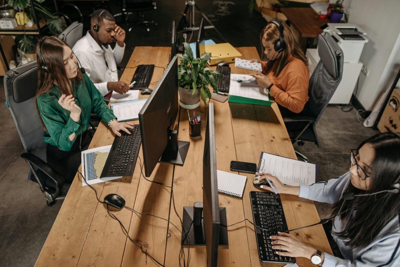 A team of call centre workers wearing headsets, working at their desks with computers and documents