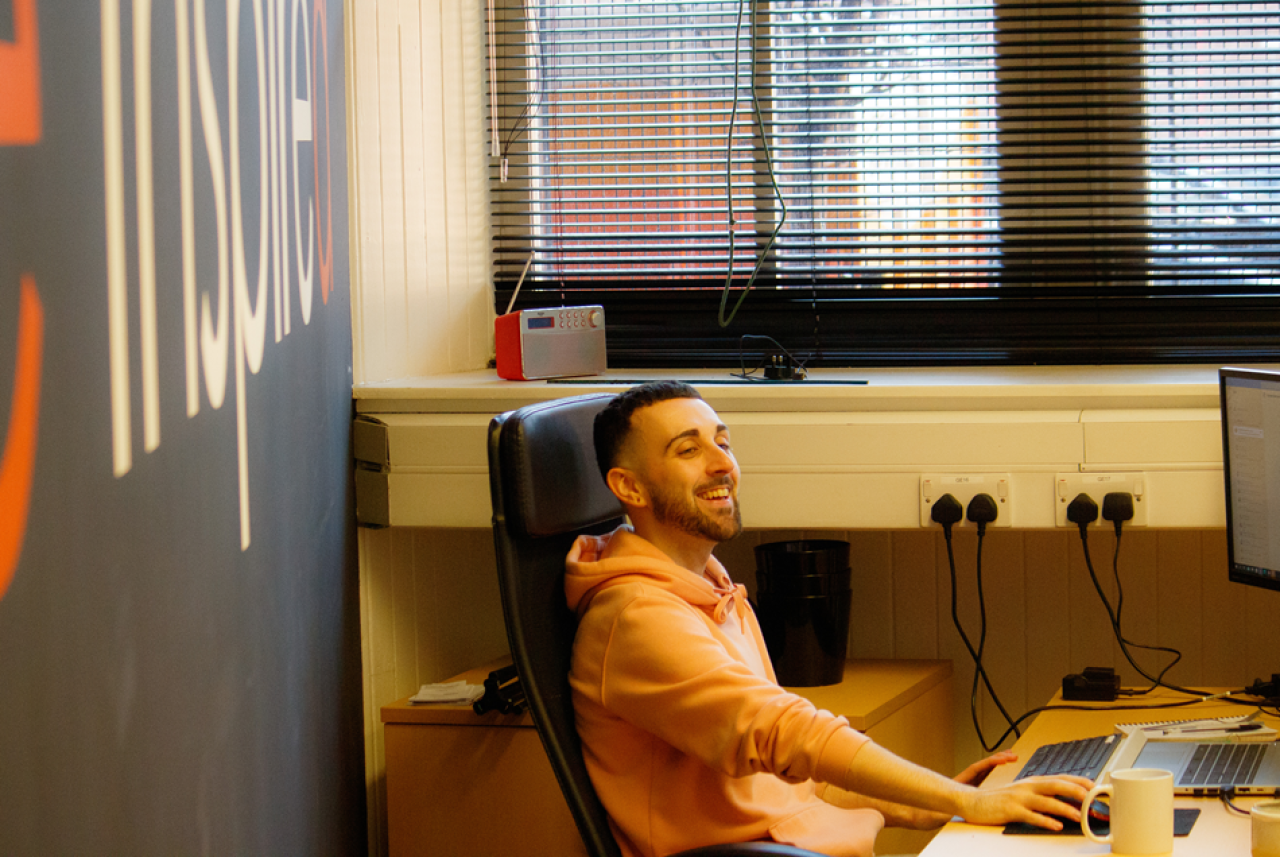 Person seated in office chair working at computer desk with large Inspire logo on the wall behind