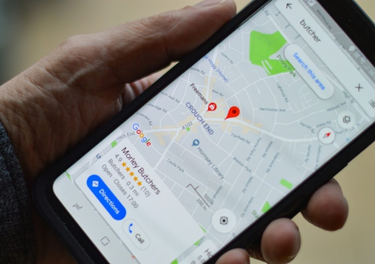 Hand holding mobile phone displaying Google Maps with a local business listing for Morley Butchers, showing rating, distance, open status, and contact options