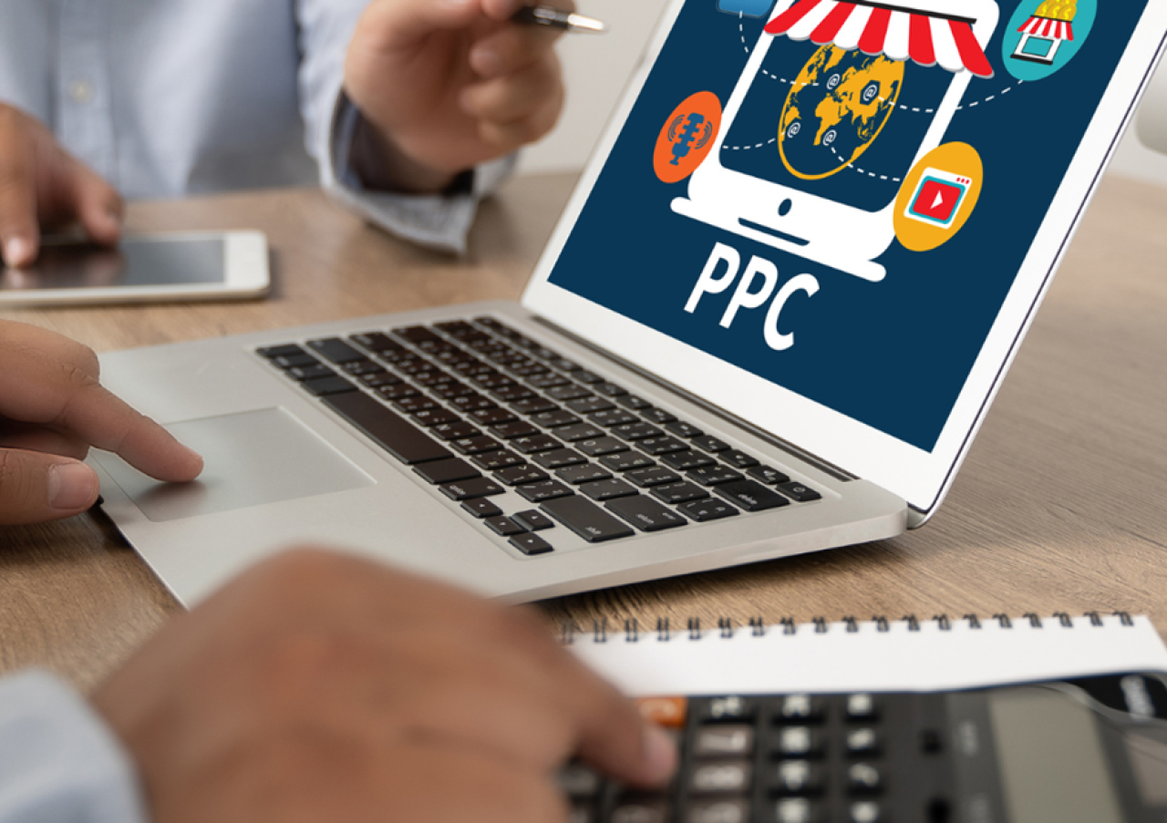 Laptop screen displaying a PPC graphic with icons next to a person using a calculator and another person holding a pen