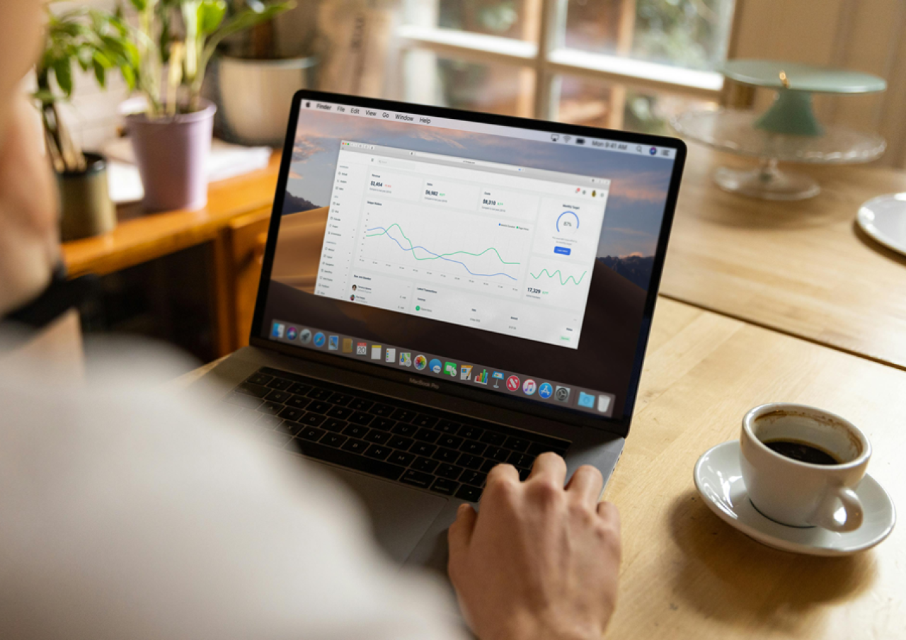 Person working on a laptop displaying SEO analytics dashboard with charts and graphs, with a cup of coffee on a wooden table