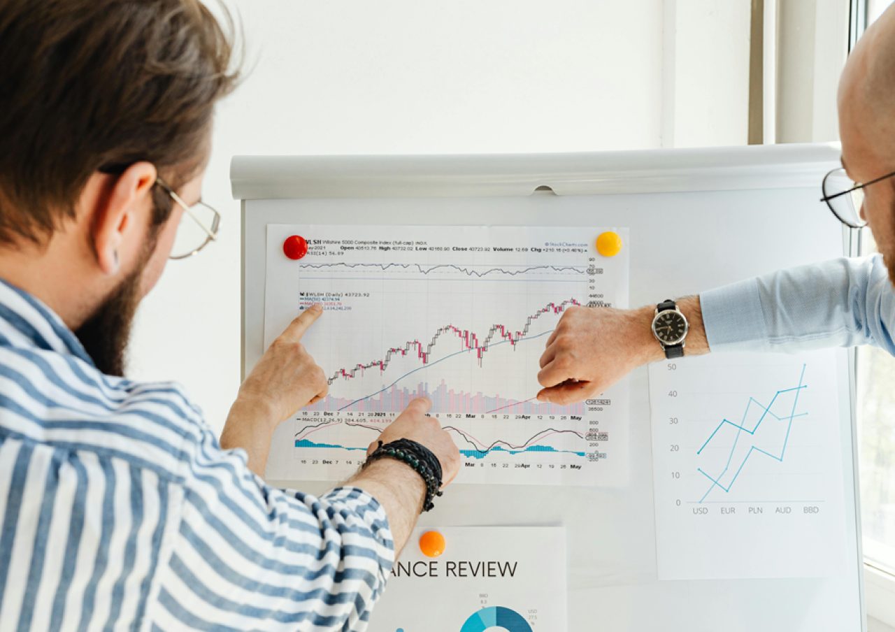 Two people reviewing charts and statistics on a whiteboard during a business meeting.