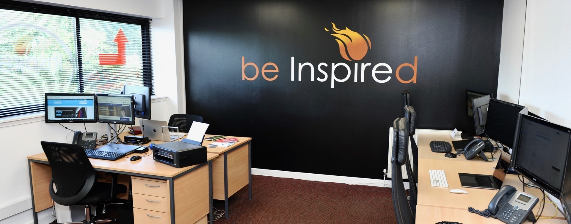 Modern office interior at Inspire Perth with workstations, computers, telephones and a black wall displaying the slogan 'be Inspired'