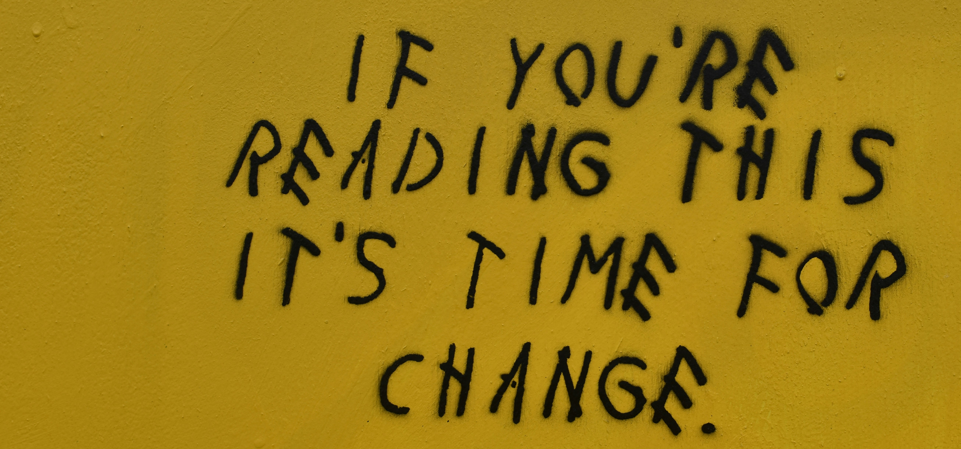 Black graffiti text reading 'If you're reading this it's time for change' on a yellow painted wall