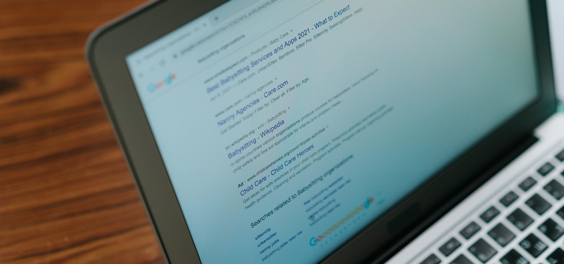 Laptop screen showing Google search results page with listings for babysitting services and related search suggestions