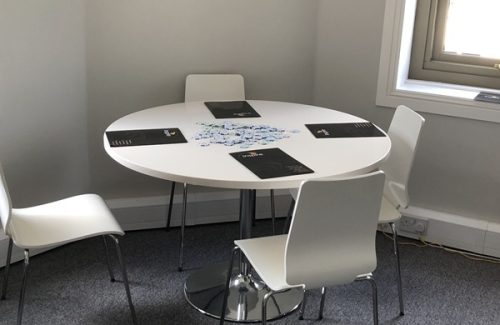 Round white meeting table with four white chairs around it in an office, with Inspire brochures on the table and a window in the background