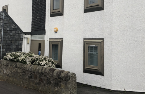 Exterior view of the Inspire Edinburgh office showing white walls, brown-framed windows, and a stone wall with white flowering plants