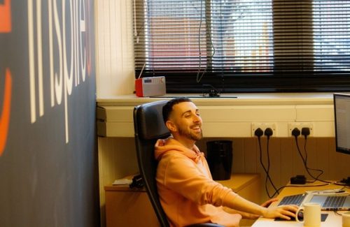 Smiling team member in an office chair working at a desk with computer screens and a mug, Inspire Glasgow office environment