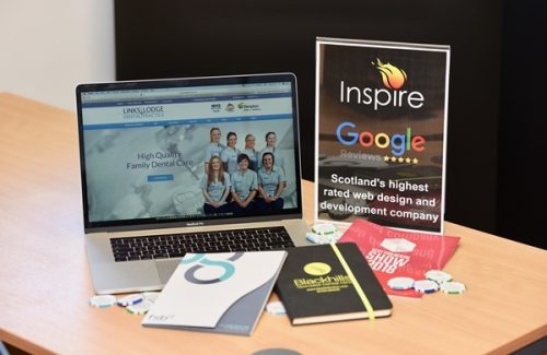 Office desk with laptop displaying Links Lodge Dental Practice website, brochures, branded notebook and a sign for Inspire with Google reviews highlighting Scotland's highest rated web design company