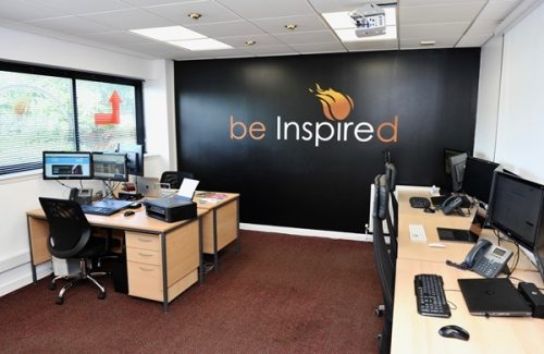 Interior view of Inspire Perth office showing empty desks, computer monitors, chairs and a wall with the ‘be Inspired’ logo