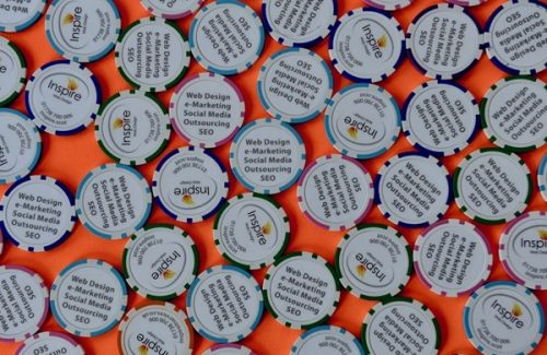 Multiple poker chips with Inspire branding and text mentioning web design, e-marketing, social media outsourcing and SEO on an orange background
