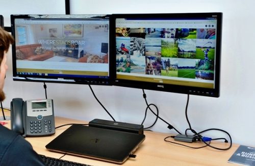 Modern office desk setup featuring dual BenQ monitors, a laptop dock, VoIP desk phone and a person working at the desk